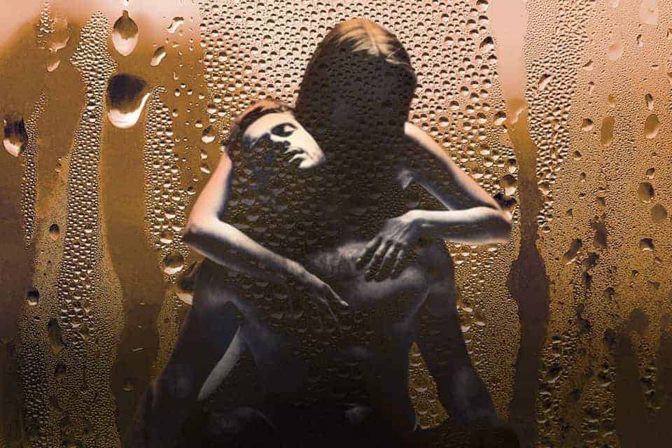 Pareja abrazándose detrás de cristal empañado.